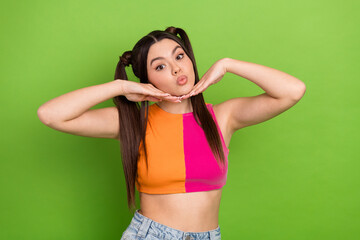 Trendy young woman with ponytails posing playfully in bright summer casual attire against a green...