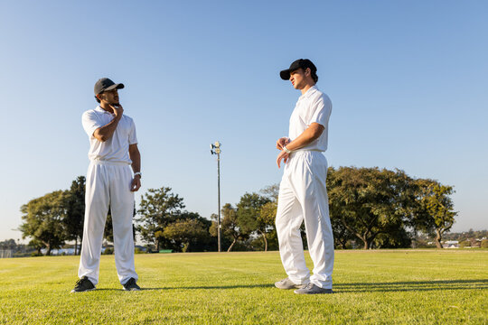 Diverse male teammates standing on pitch under floodlight tower adjusting wristwatch and cap