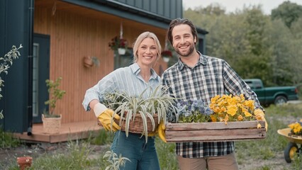 Portrait of Caucasian loving couple with gardening gloves holding blooming flowers and plants....