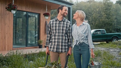 Caucasian couple looking at each other with love. Happy people holding gardening equipment. Preparing to planting plants and herbs near their house. Enjoying working together. Farming concept.