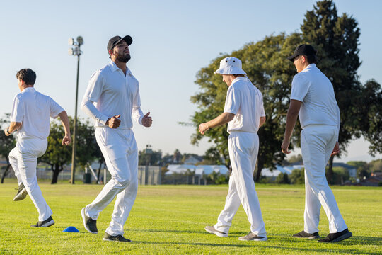 Male cricket teammates performing warm-up drills on suburban practice ground around blue cones