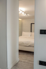 Minimalist bedroom interior with white bed and white brick wall, seen through a modern doorway. Bright lighting and clean design create a serene, cozy atmosphere