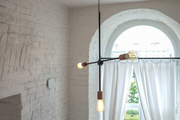 Minimalist loft interior with industrial chandelier and large arched window. White brick walls and...