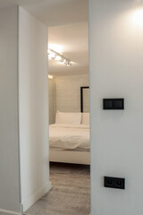 Bright minimalist bedroom with white walls and bed, visible through a doorway. Soft lighting and modern decor create a peaceful and airy interior atmosphere
