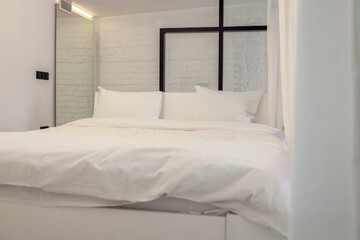 Minimalist bedroom with white bedding and industrial-style glass partition. Soft lighting and white...