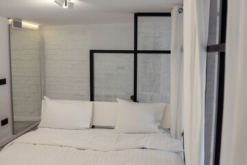 Minimalist bedroom with white bedding and industrial-style glass partition. Soft lighting and white...