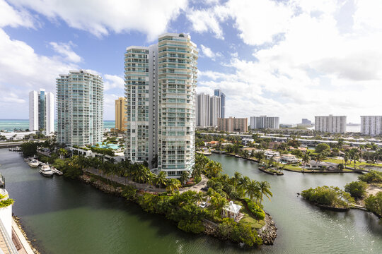 Aerial view of gleaming white high-rise condos reflect the azure sky, juxtaposed against the dark green waterways and verdant isles, Aventura, Florida, United States.