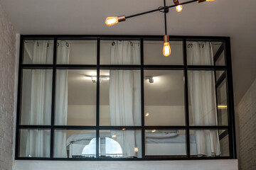 Modern loft bedroom with large glass wall and black metal frame, soft curtains, and minimalistic...