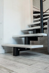 Close-up of modern minimalist staircase design with white wooden steps and black metal supports....