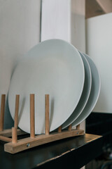 Close-up of white ceramic plates neatly arranged on a minimalist wooden drying rack. Simple and stylish kitchenware detail emphasizing cleanliness and organization