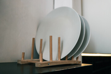 Close-up of white ceramic plates neatly arranged on a minimalist wooden drying rack. Simple and...