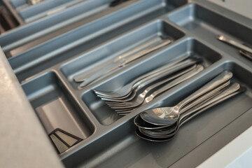 Drawer with neatly arranged cutlery, including spoons, forks, and knives, stored in a gray plastic...