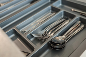 Close-up of neatly organized stainless steel forks, spoons, and knives in a gray kitchen drawer...