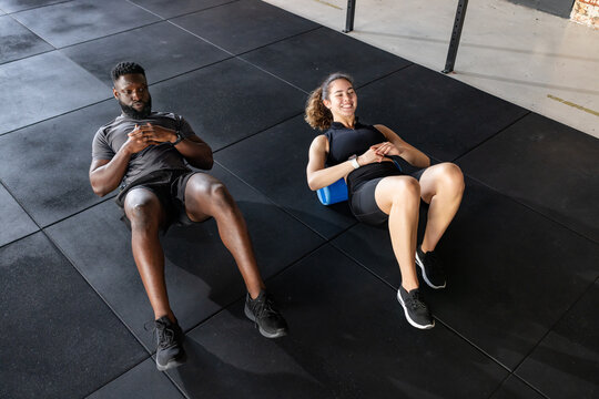 Diverse workout partners lying on foam rollers in sportswear exercising at gym with smartwatches - Powered by Adobe