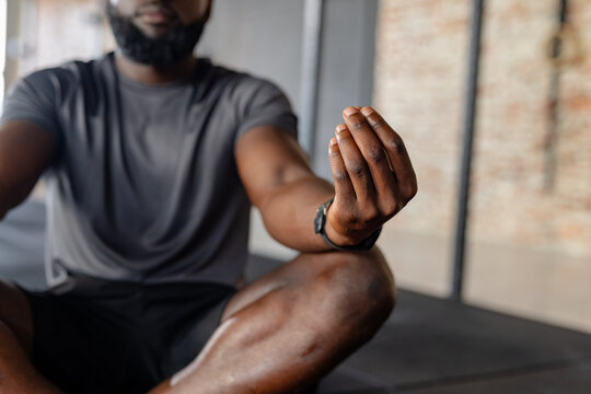 African American man meditating cross-legged on mat in gym wearing sportswear and smartwatch