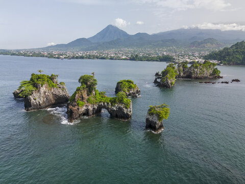 Aerial view of Bota Island's rugged cliffs and vibrant greenery meet the ocean, with the city and Mount Cameroon in the distance, Limbe, South West, Cameroon.