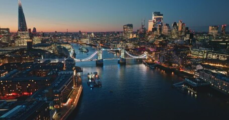 Illuminated Tower Bridge and The Shard glow in evening twilight, framing vibrant London skyline above the River Thames. Bright night lights, modern city architecture cityscape. Drone flight footage - Powered by Adobe
