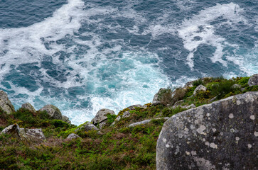 Dramatic top view of ocean waves hitting rugged rocks and green cliff, showcasing natural beauty and coastal wilderness. Ideal for travel, nature, and landscape themes.