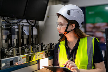 A woman wearing a yellow vest and a white helmet is looking at a tablet. Female engineer working...