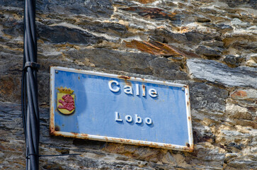 Vintage blue street sign Calle Lobo with a Spanish crest mounted on an old textured stone wall, capturing authentic local atmosphere in a Spanish village.