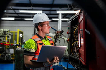 A man wearing a yellow and green vest is looking at a laptop. Electrical engineer or technician...