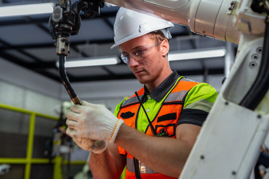 A man in a yellow and green vest is working on a machine. Robotics engineer performing maintenance and calibration on an automated robot arm in a smart factory.