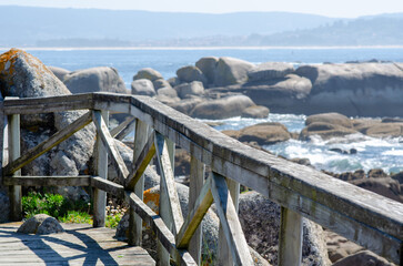 Scenic wooden boardwalk by the seaside, offering a peaceful view of rocks and crashing ocean waves, ideal for travel, relaxation, or nature concepts.