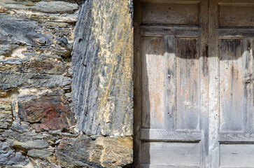Close-up of an old wooden door framed by textured stonework, evoking rustic charm and historical village atmosphere. Perfect for backgrounds and architectural themes.