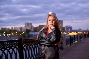 A woman in a red dress goes along the embankment. It has a black jacket. The action takes place at...