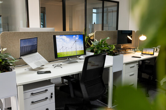 Workspace featuring monitors showing wind turbines, with devices, decor, seating by fabric divider