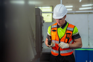 A man in a safety vest is wearing a hard hat and holding a cell phone. Machinist or CNC machine...