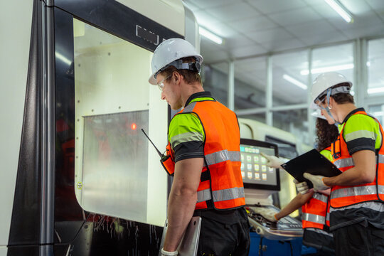 A man in a yellow vest is standing in front of a machine. Group of diverse engineers collaborating and communicating on a production line in an industrial plant. - Powered by Adobe