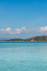 Turquoise sea with distant forested island, boats, and blue sky in tropical Labuan Bajo scenery