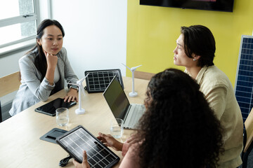 Diverse coworkers discussing wind turbine models and tablet showing solar panel at meeting table
