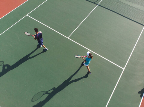 Doubles partners preparing to return shot on hard court under bright sunlight with rackets and net