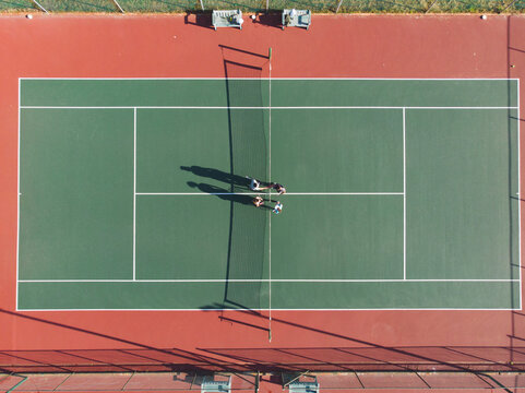 Diverse tennis players gathering at net on outdoor court holding rackets and water bottles
