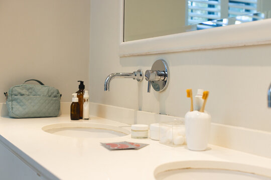 Twin oval sinks are sitting on countertop under faucets, toiletry bag and toothbrushes under mirror