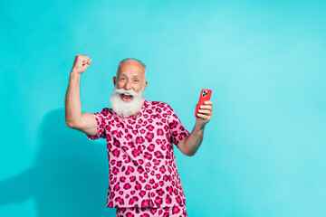 Photo of attractive senior bearded man hold device winning dressed stylish pink leopard print clothes isolated on cyan color background