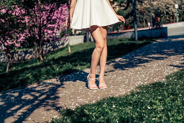 Young woman in a white dress enjoying springtime in a sunny blooming park setting during a...