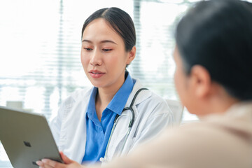 Asian female doctor conducts thorough medical consultation with elderly Caucasian patient, actively...