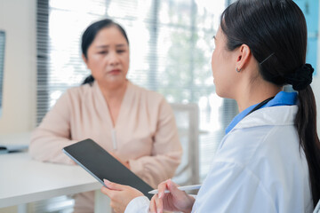 Asian female doctor conducts thorough medical consultation with elderly Caucasian patient, actively...