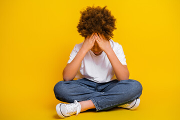 Young boy sitting against a vibrant yellow background showing thoughtfulness and emotion
