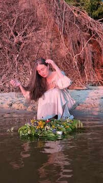 Ukrainian girl in wreath poses near water.
