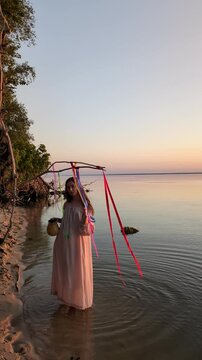 Ukrainian girl in wreath poses near water.
