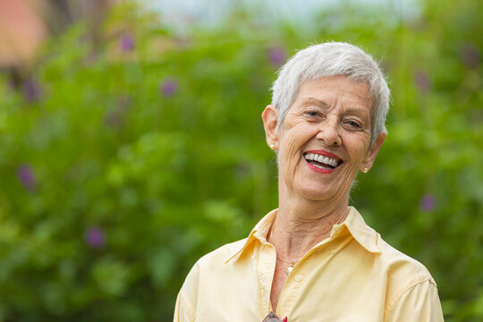 Smiling senior woman with gray hair in yellow shirt outdoors