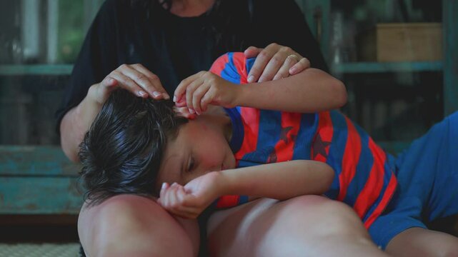 Child burying face in mother&rsquo;s lap while being comforted with soft caress, quiet indoor setting highlighting soothing connection and emotional security