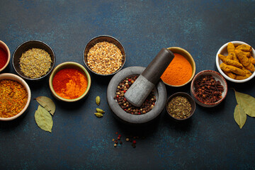 Colorful bowls of aromatic spices and herbs on a dark background, with a mortar and pestle, creating a border. Top view of flavorful ingredients for gourmet cuisine
