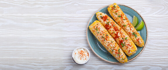 Three grilled corn cobs coated in spices, mayonnaise, and cotija cheese are served on a plate with...