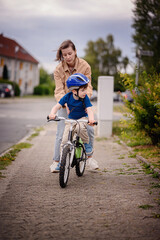 Woman Helping Young Boy Learn to Ride Bike on Sidewalk