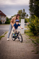 Woman Helping Young Boy Learn to Ride Bike on Sidewalk